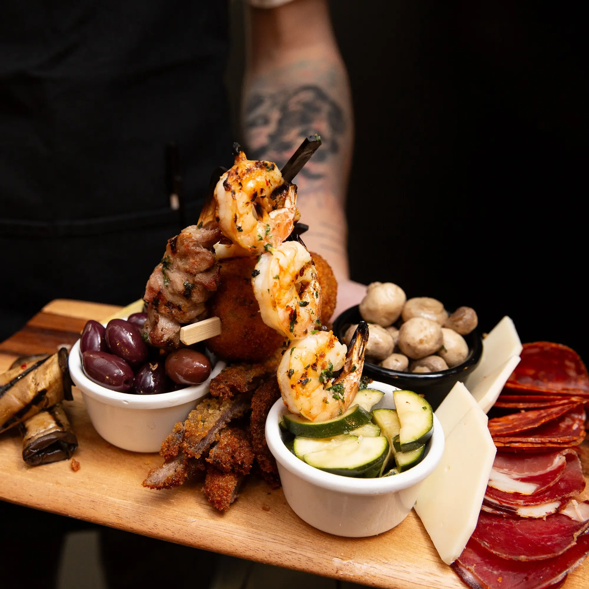 Antipasti on a plate being held up by a man with tattoos on his arm.