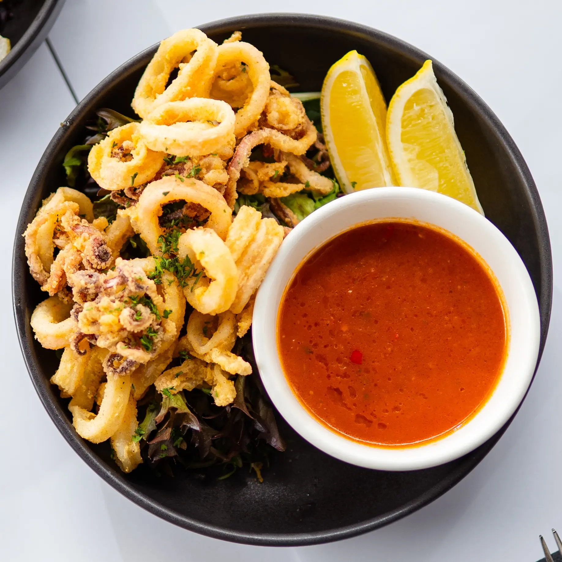 A plate of calamari with a side of lemon and chilli sauce.