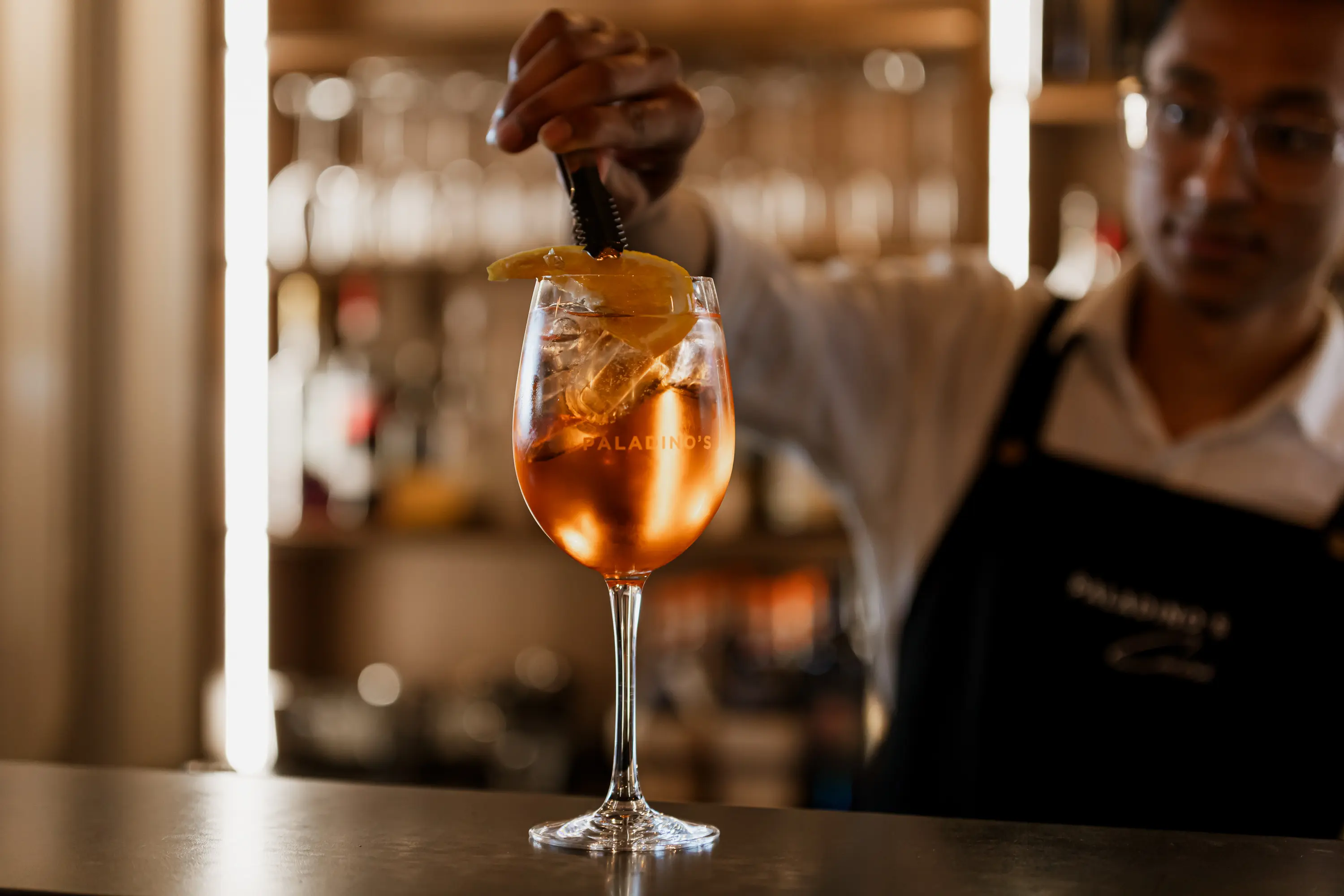 A glass of spritz in a glass with the logo of Paladino's Cucina.